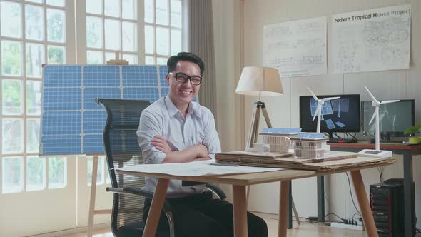 Asian Man Cross Arms And Smile To Camera While Working With A Blueprint And The Model Small House