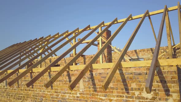 Aerial view of unfinished brick house with wooden roof structure under construction.