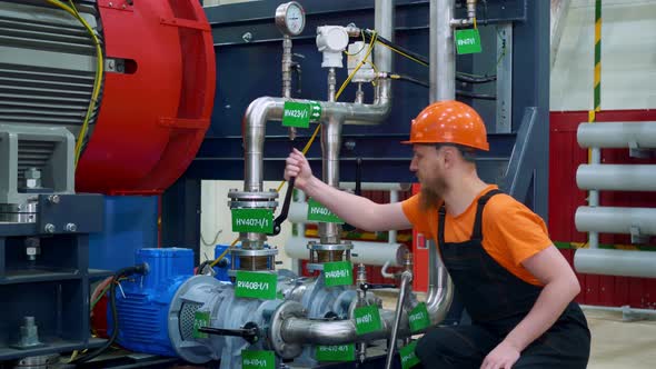 A Bearded Worker in a Helmet Closes a Valve to Prevent an Industrial Accident