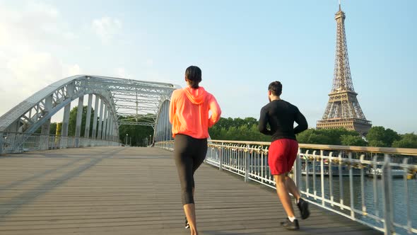 A man woman couple running across a bridge with the Eiffel Tower