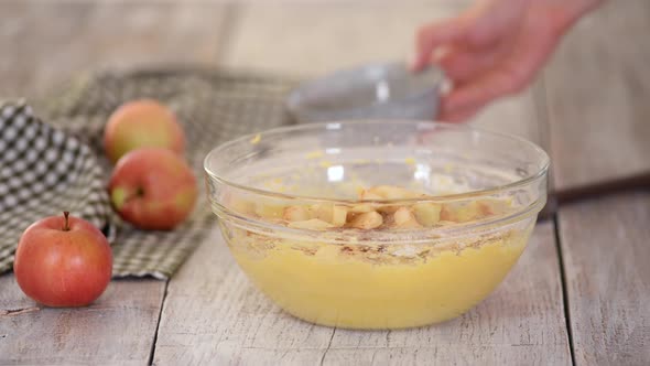 Woman Adding Chopped Apples To Batter and Use a Rubber Spatula To Fold the Apples Into the Batter.