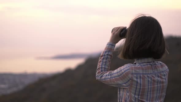 Young Woman in the Mountains Looks Through Binoculars