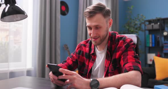 A Handsome Young Man Sits at a Desk in a Room and Uses the Phone