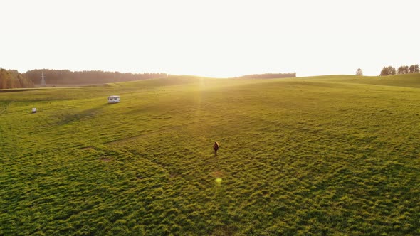 Aerial View of Young Girl Running Through Green Hilly Meadows with Her Arms Open Out Against Sunset