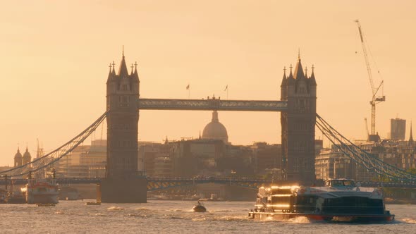 Late afternoon light behind Tower Bridge, London, UK. A ferry crosses in front whilst the dome of St