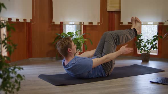 Male Practicing Online Yoga Abs Exercises on Floor Mat Using Laptop in Living Room at Home