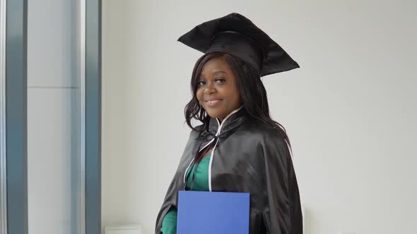 An African American Female Graduate in a Classic Master's Suit and Mantle Stands with a Diploma in