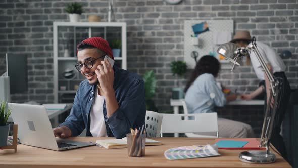 Business Owner Making Call with Smartphone Sitting at Desk in Creative Office