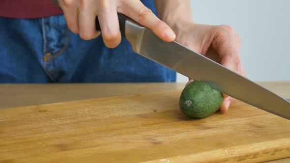 Female Hands is Cutting a Fresh Green Feijoa Fruit on a Cut Wooden Board