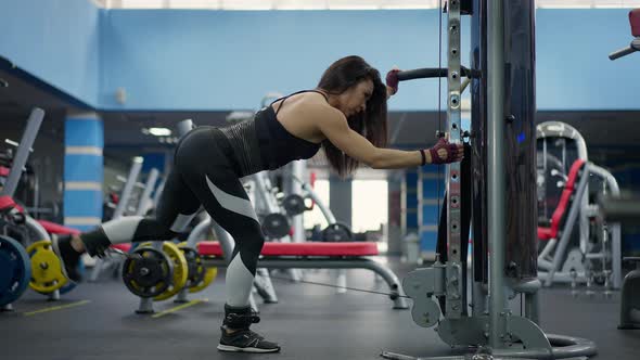 Wide Shot of Strong Motivated Caucasian Sportswoman Training Leg Muscles Pulling Resistance Weights