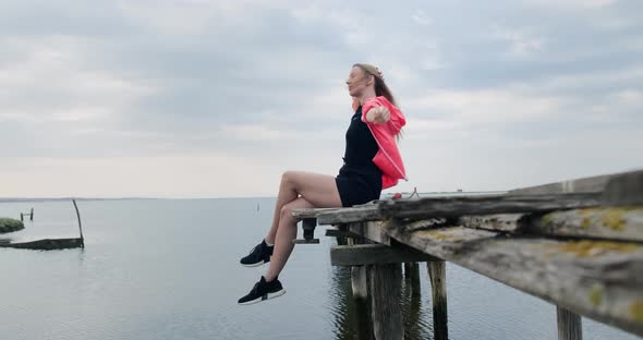 Woman sitting with her legs dangling on old wooden pier.