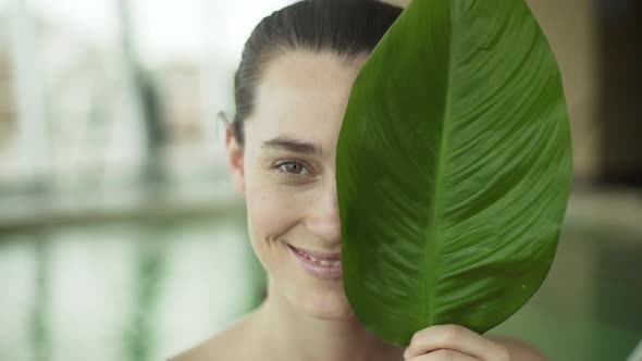 Young woman holding large leaf in front of her face and smiling