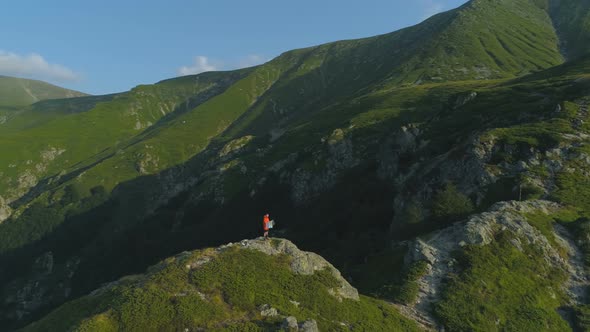 Drone View of Lonely Hiker Holding a Map Sitting on Rocky Edge at the Top of the Mountain