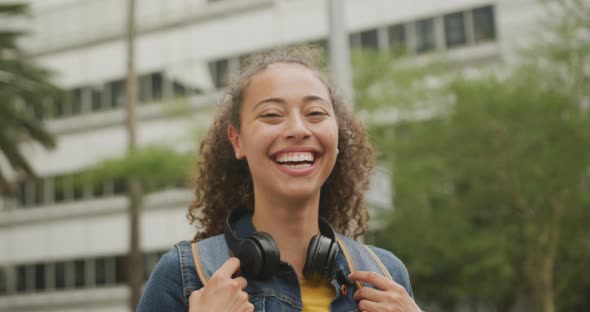 Portrait of happy biracial woman in city, wearing headphones and smiling