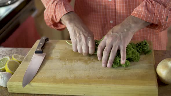 Camera slides from right to left as a chef prepares a pile of parsley and chops it while cut lemons