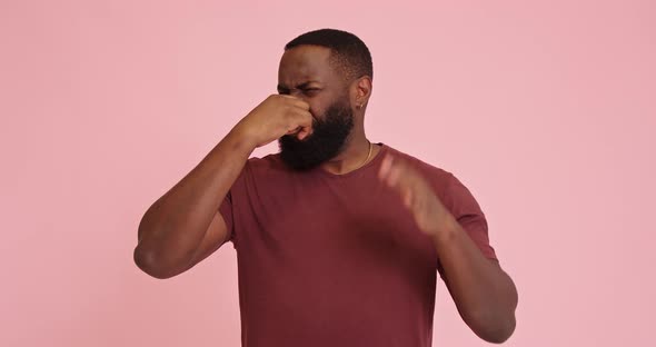 Young African American Man on Pink Background Holding Breath with Fingers on Nose