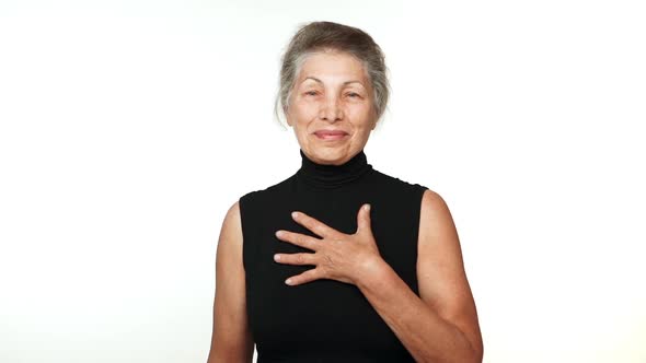 Elder Serene Woman with White Tied Hair Looking at Camera Smiling with Hand on Chest Thanking Over