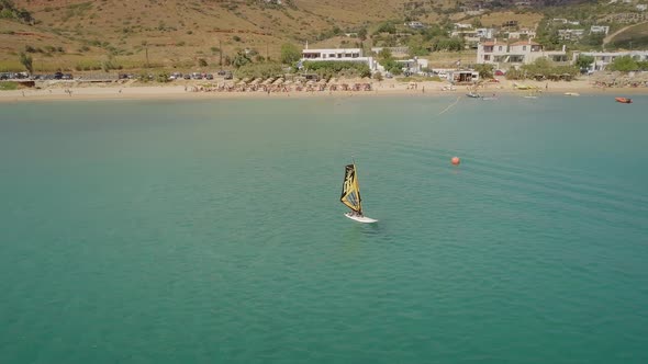 Aerial view of young boy raises windsurfing sail at a beach in Greece.