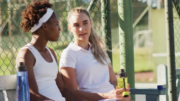 Video of happy diverse female tennis players sitting, talking and resting after match