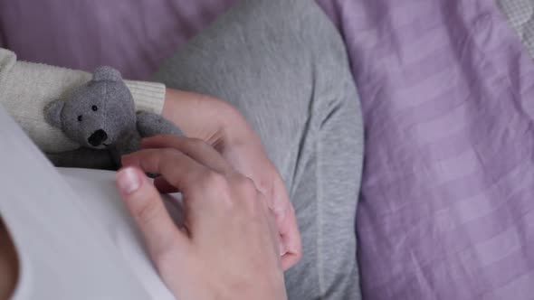 Pregnant Girl in White T-shirt Sitting on the Bed and Holding