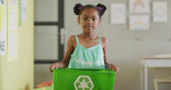 Video of happy african american girl holding box with recycling symbol in classroom