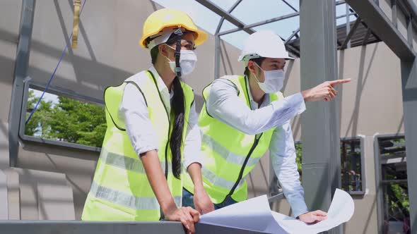 Asian construction workers people wearing protective face mask onsite and holding blueprint drawing.