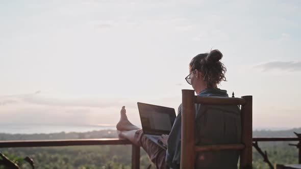 Freelancer woman sits with a laptop on a high bar chair. 