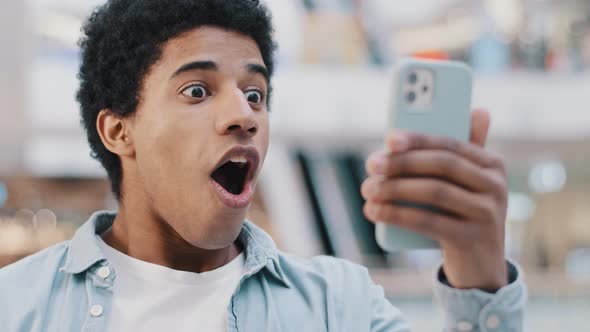 African American Surprised Shocked Amazed Man User Guy Teenager Looking at Mobile Phone Opens Mouth