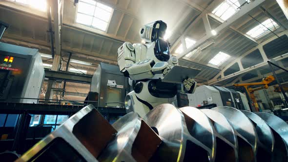 Robot Checks Metal Detail at a Factory, Typing on a Tablet.