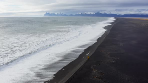 Drone Over Black Sand Beach With Mountain Range In Background