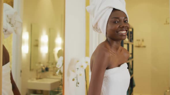 Portrait of smiling african american woman next to mirror with towel in bathroom