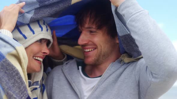 Happy couple hiding in blanket at beach