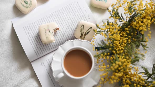 Top view of eating easter treats and coffee while reading a book with beautiful yellow flowers on a