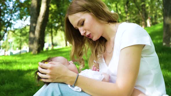 Cute Little Baby Sleeping on Lap of Young Mother Sitting in Park