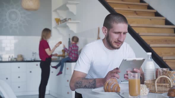 Portrait of Caucasian Young Businessman Using Tablet As Blond Woman and Little Girl Preparing