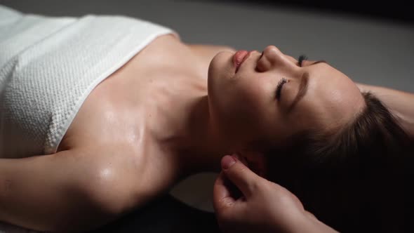Closeup of Male Masseur Massaging Auricle of Young Woman Lying Down in Massage Table at Spa Salon