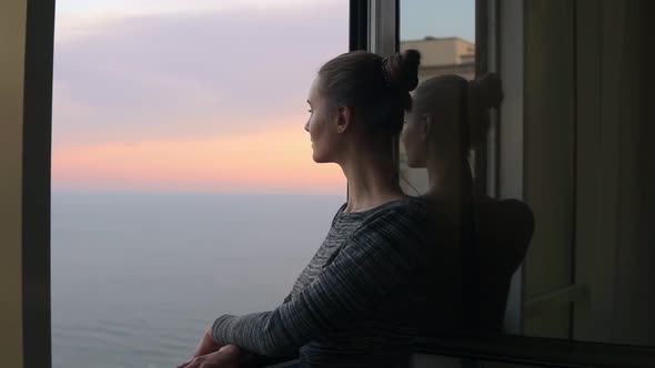 Closeup View of Beautiful Young Woman Standing By the Open Window During the Sunset By the Sea and