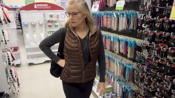 Pretty blonde, mature woman walking through aisles of beads and earrings in a craft store.