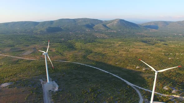 Flying above two elegant white wind turbines on green hills