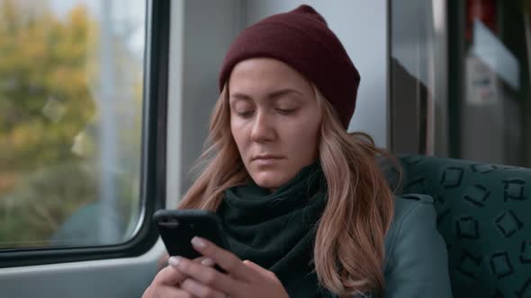 Young Caucasian Girl in a Red Cap Rides on a Subway or Tram Train Car, Uses the Phone