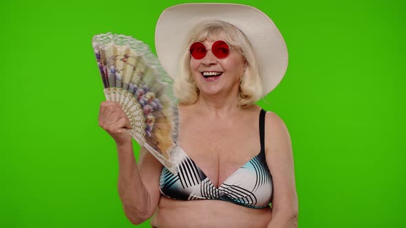 Senior Old Woman Tourist Exhales From Heat or Stuffiness Waves Hand Fan at Herself on Chroma Key