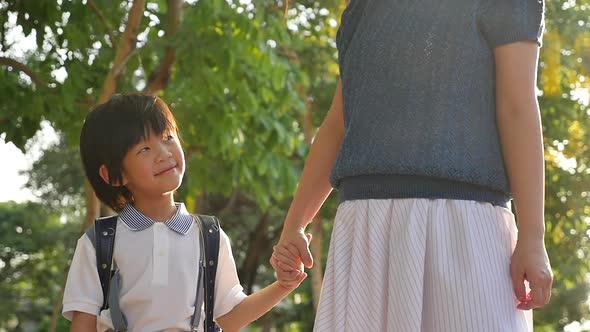 Asian mother holding hand of little son with backpack outdoors, back to school slow motion