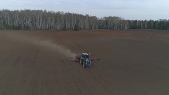 A tractor plows in a huge field on the background of the forest