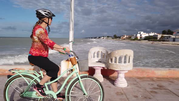 Closeup of mature woman riding cruiser bicycle on a pier with a sea in the background.