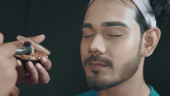 Close up of man's face in cosmetics studio and make up artist putting powder on his face