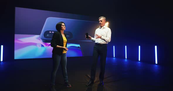 Male and Female Speakers Showing Smartphone on Stage