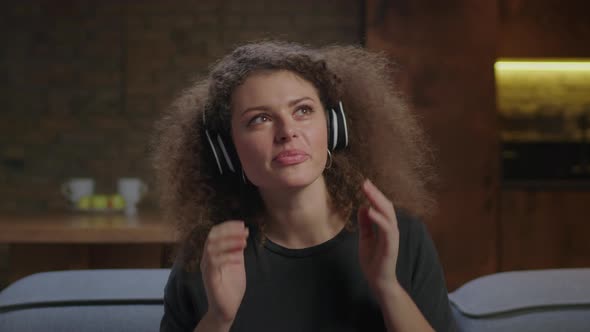 Young Woman Listening Music in Wireless Headphones with Closed Eyes Sitting on Couch at Home