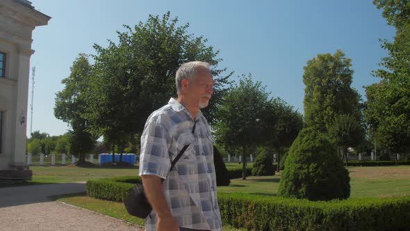 Grey Haired Old Man Walks Along Green Park Zone Against Sky