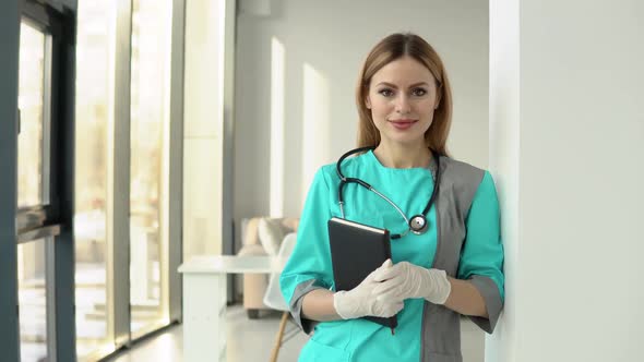 A Woman Doctor Wearing Medical Coat and Stethoscope with Documents in Her Hands Looking at Camera
