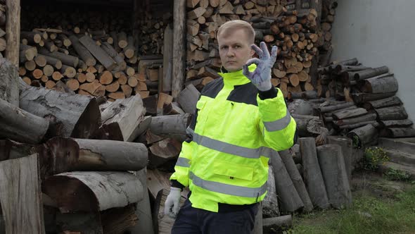 Lumberjack in Reflective Jacket, Man Woodcutter Show Ok Sign, Sawn Logs, Firewood Background